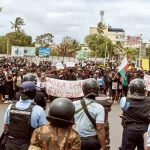 Protesters wave flags in Antananarivo as riot police stand guard during Madagascar protests demanding Rajoelina resignation.