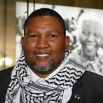 Mandela’s grandson walks with wife at Johannesburg airport after deportation, greeted by supporters waving Palestinian flags and banners.