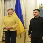 Zelenskyy and Latvia's foreign minister shake hands and smile for the camera during official meeting in Kyiv.
